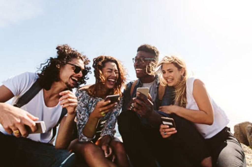 Neljä hyväntuulista ihmistä rinnakkain katsomassa yhden puhelinta yhdessä